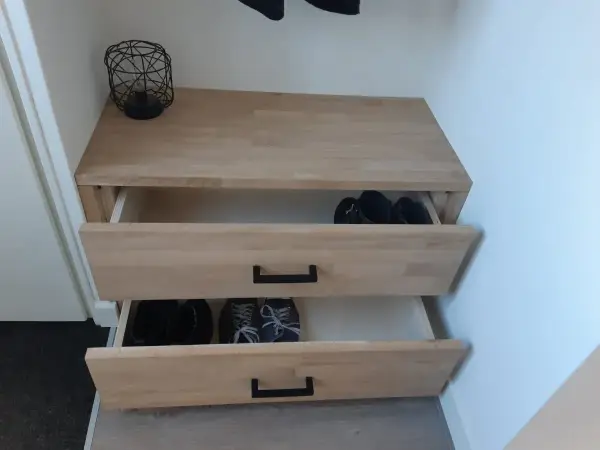 Meuble à chaussures fait maison en bois clair, avec deux tiroirs ouverts contenant des bottes et des baskets.